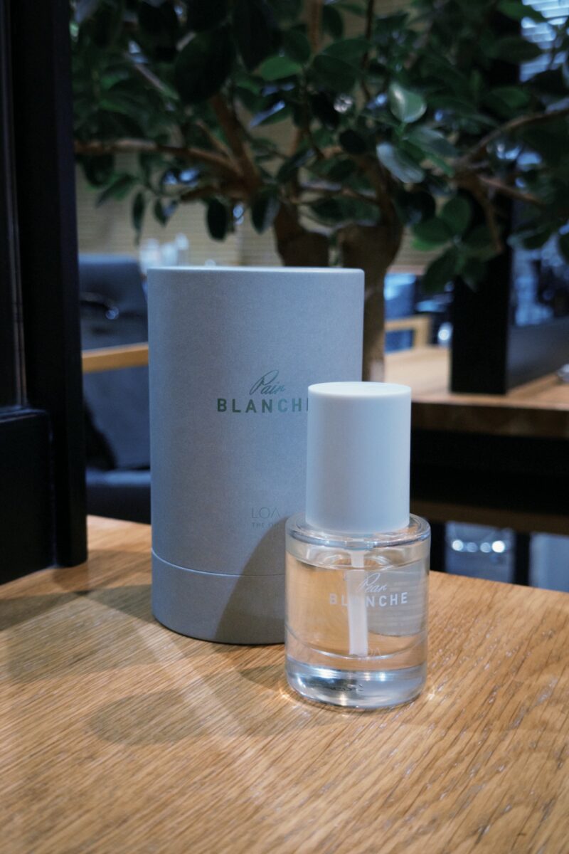 木目テーブルに置かれたロアオイルとグレーのパッケージ、観葉植物のある店内