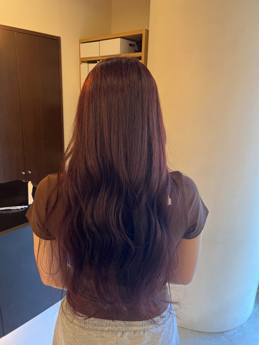赤みを重ねた艶やかなロングヘアの後ろ姿、緩やかな波巻きスタイル