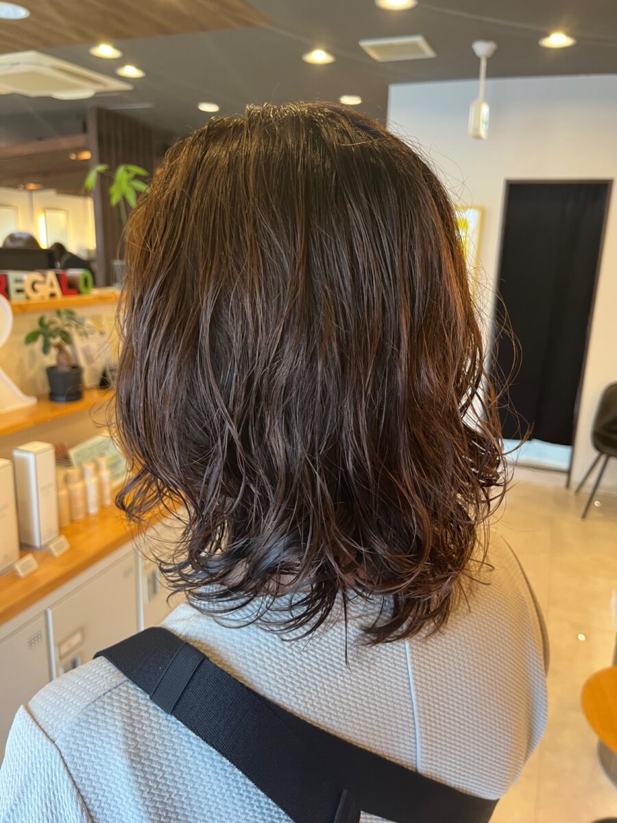ウェット感のあるスパイラルウェーブが揺れる艶やかなミディアムヘアの後ろ姿