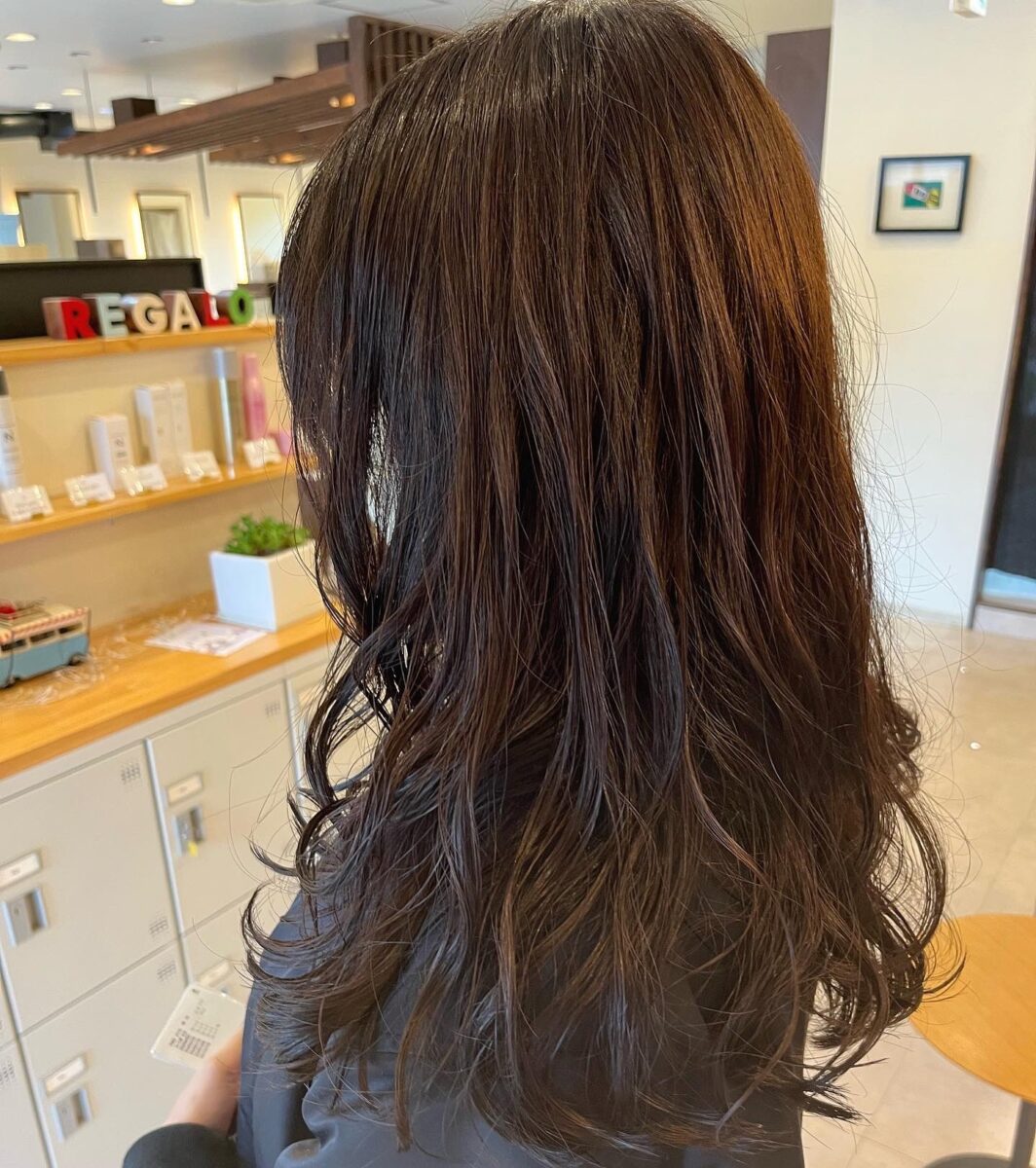 茶色がかったゆるやかなウェーブヘアをサロン店内で後ろから撮影